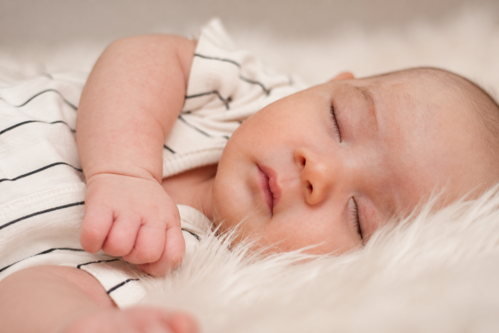 Close-up of a sleeping baby with one hand beside their face.