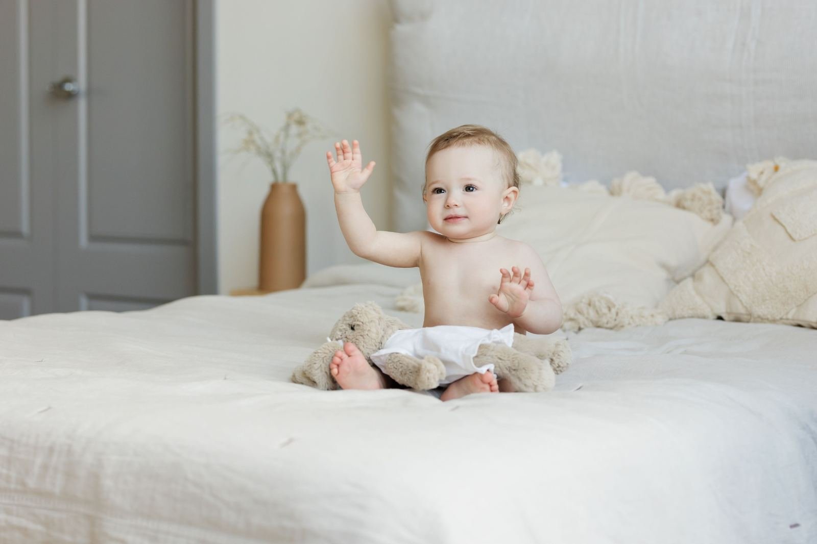 Baby sitting on a bed, raising one hand