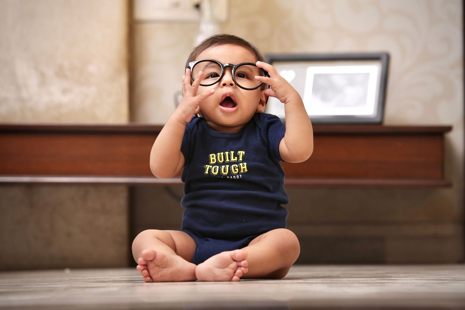 Baby sitting on the floor while holding oversized glasses